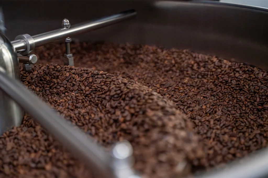 Vers gebrande koffiebonen die afkoelen in een koffiebranderij koeltrommel bij Lorando & Morini.