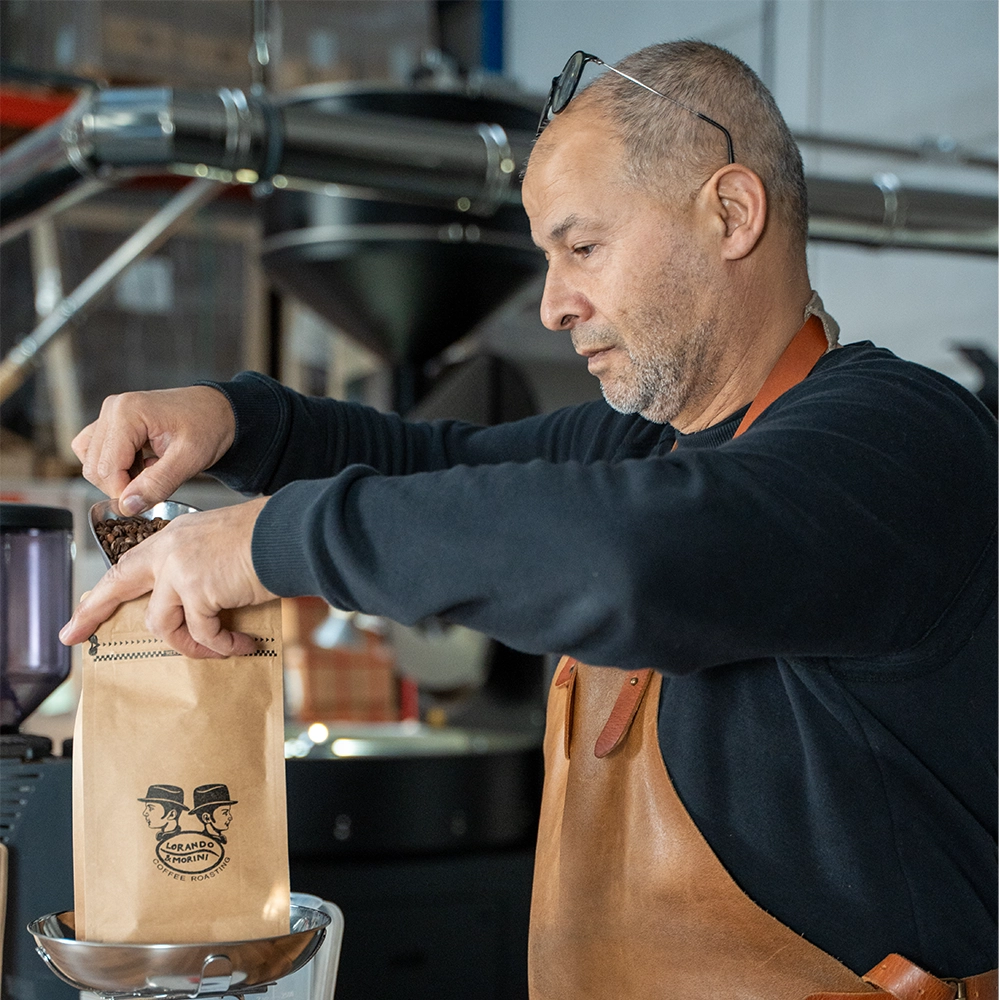 Dos van Lorando & Morini vult een koffiezak met vers gebrande koffiebonen in de branderij.