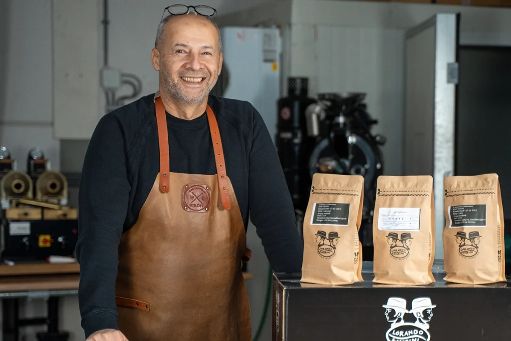 Dos van Lorando & Morini staat in de koffiebranderij naast verpakkingen met specialty koffiebonen.