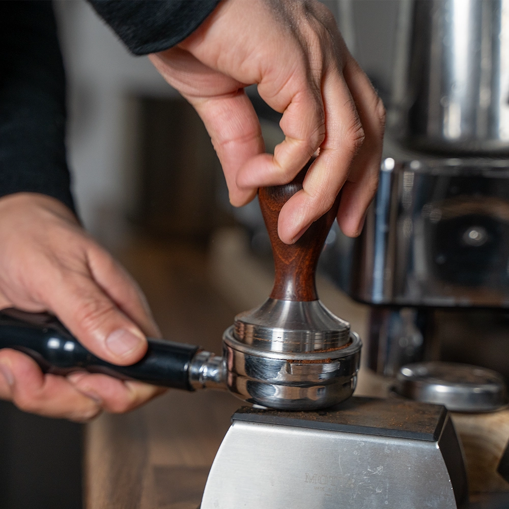 Gemalen koffie wordt met een tamper aangedrukt in een portafilter voor het zetten van espresso.