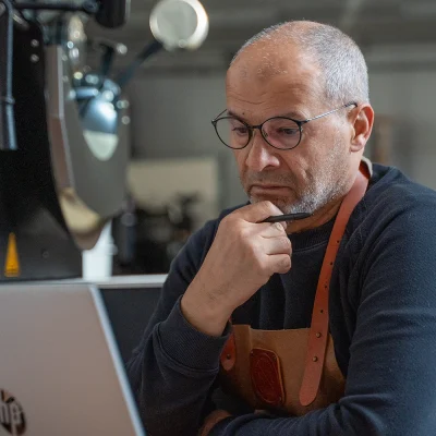 Dos van Lorando & Morini werkt op een laptop in de koffiebranderij naast de koffiebrander.